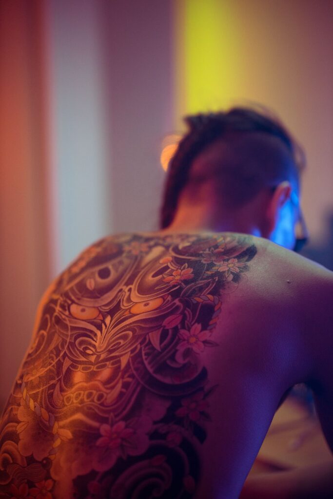 Back view of a shirtless person showcasing a large Japanese tattoo in warm ambient lighting.