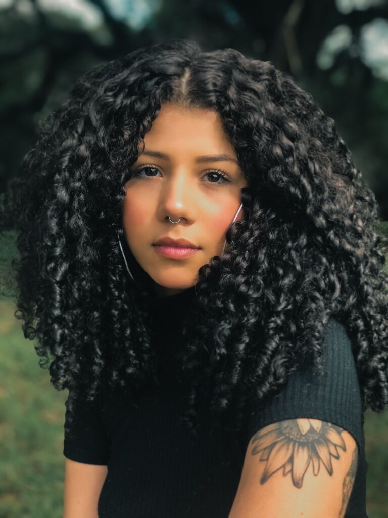 Beautiful portrait of a woman with curly hair and tattoo sitting outdoors.