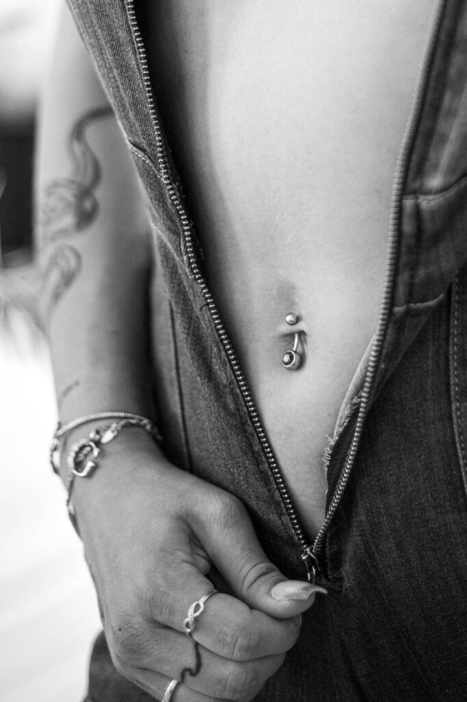 Black and white close-up of a belly piercing and tattoos with jeans details.