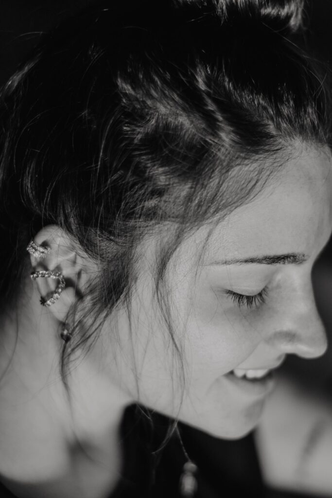 Close-up black and white portrait capturing a woman's serene smile and intricate ear piercings.