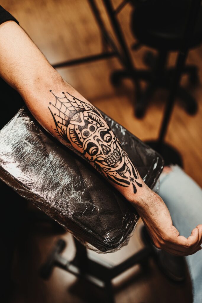 Close-up of a detailed skull tattoo on a man's forearm in a tattoo studio setting.