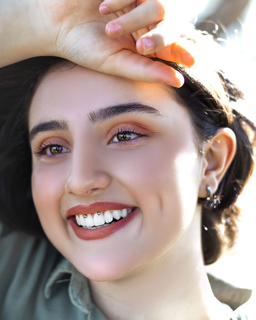 Close-up of a joyful woman with a bright smile and a hand on her forehead.