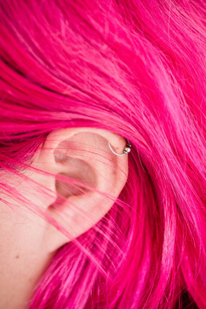 Close-up of bright pink hair and pierced ear, showcasing trendy style.