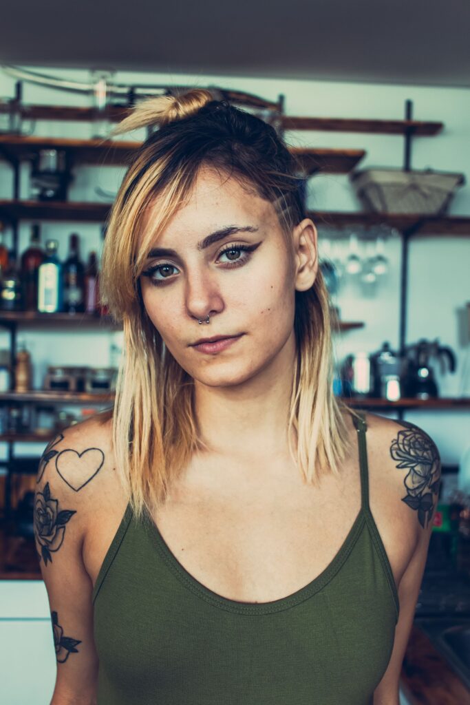 Close-up portrait of a tattooed young woman with blonde hair indoors, exuding confidence and style.