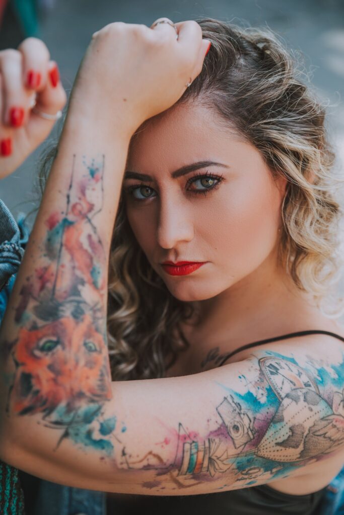 Close-up portrait of a woman showing colorful arm tattoos, with focus on expression and art.