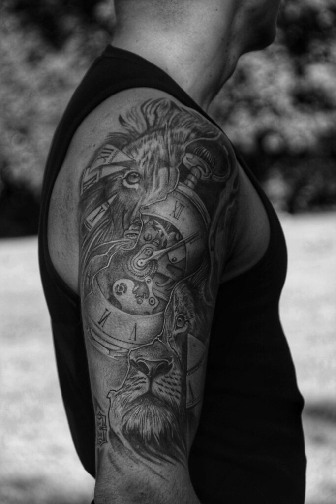 Detailed monochrome tattoo of a lion and clock on a man's arm in profile.