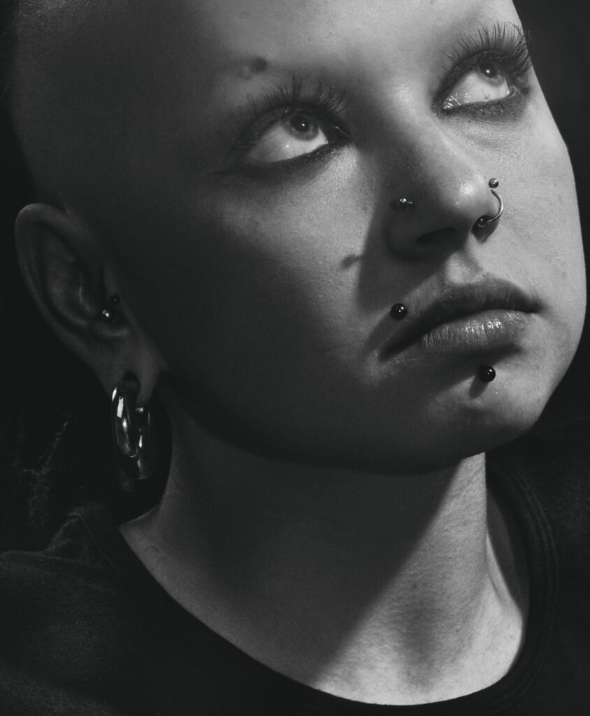 Dramatic grayscale portrait of a young woman with facial piercings.