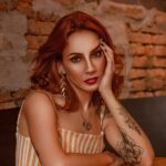Portrait of a woman with tattoos and red hair in a modern indoor setting.