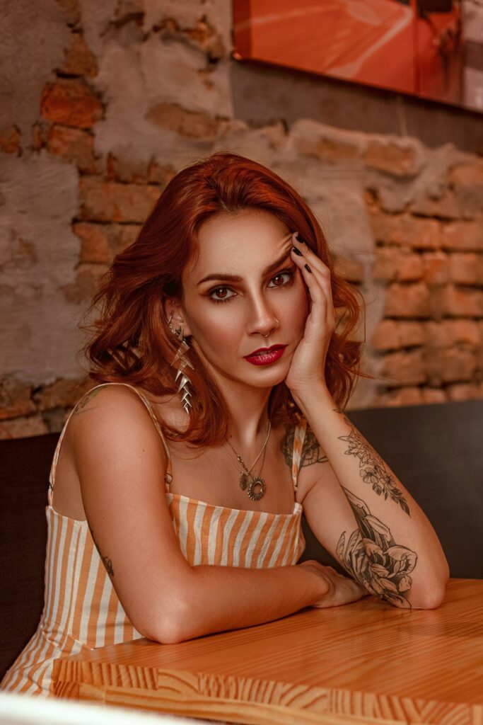 Portrait of a woman with tattoos and red hair in a modern indoor setting.