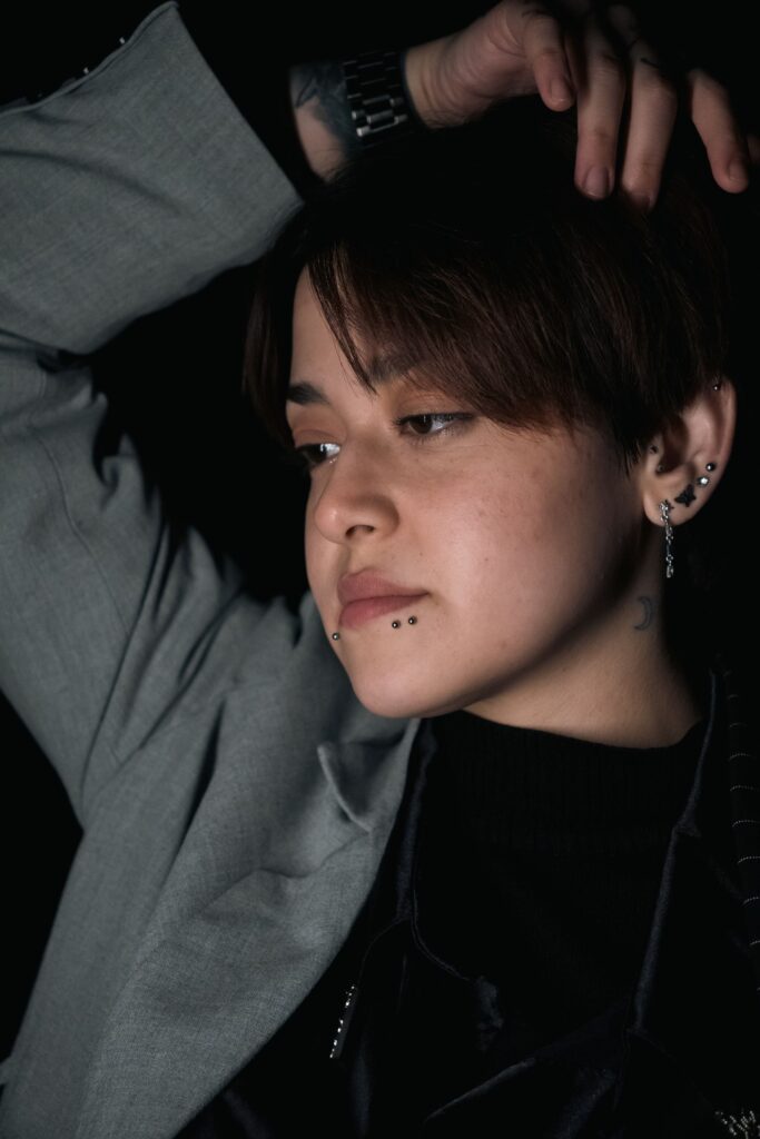 Portrait of a young individual with multiple piercings in a contemplative pose under soft lighting.