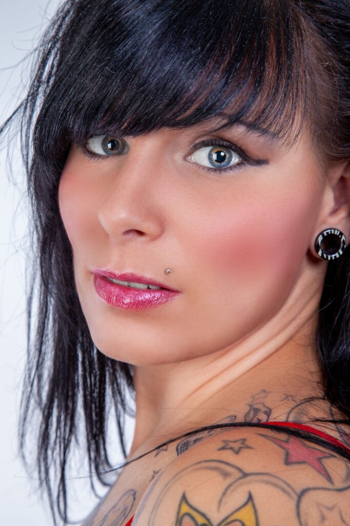 Stylish woman with tattoos and piercings, close-up portrait highlighting vivid makeup and expressive eyes.