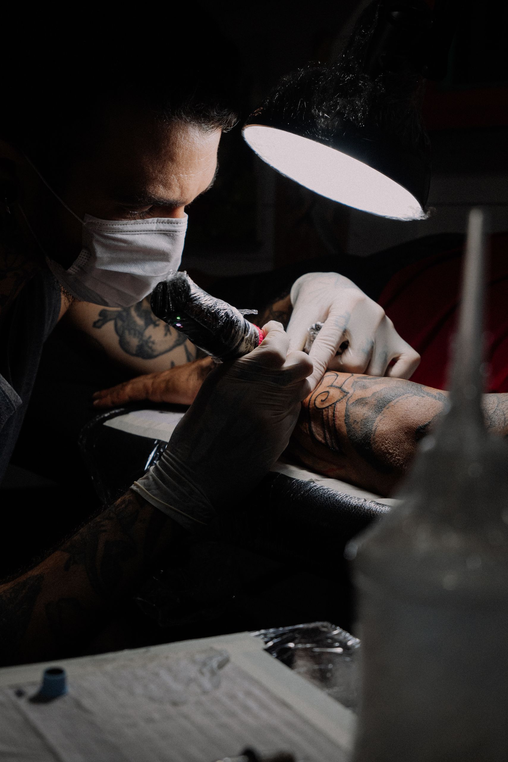 Tattoo artist focused on creating a detailed design under bright studio lighting.