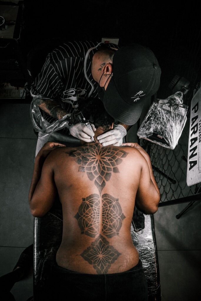 Tattoo artist working on a large geometric back tattoo in a studio setting.