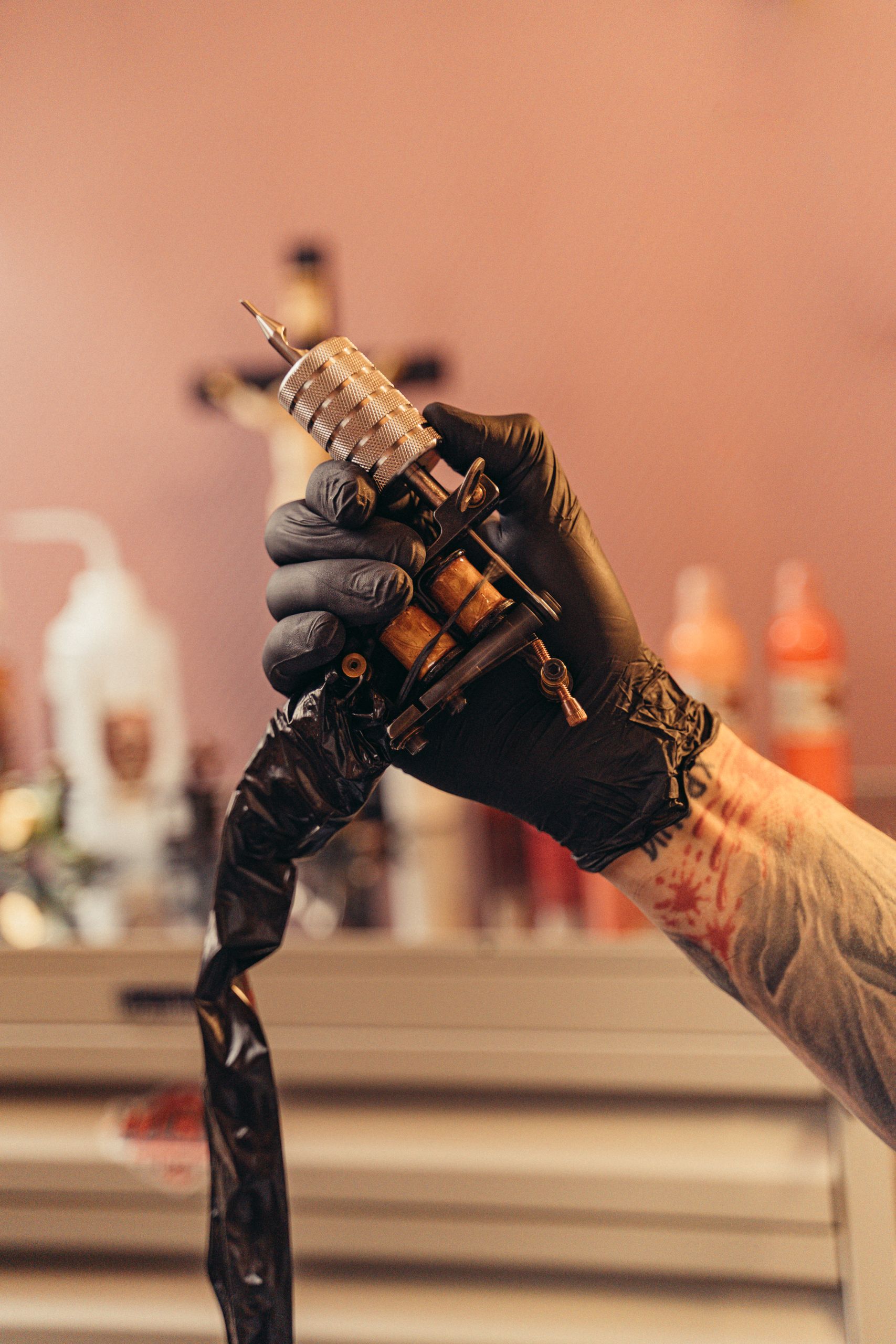 Tattoo artist's gloved hand holding a tattoo machine in a studio with blurred background.