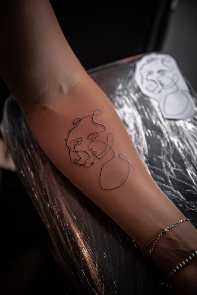 Tattoo close-up showing minimalist line art design on forearm.