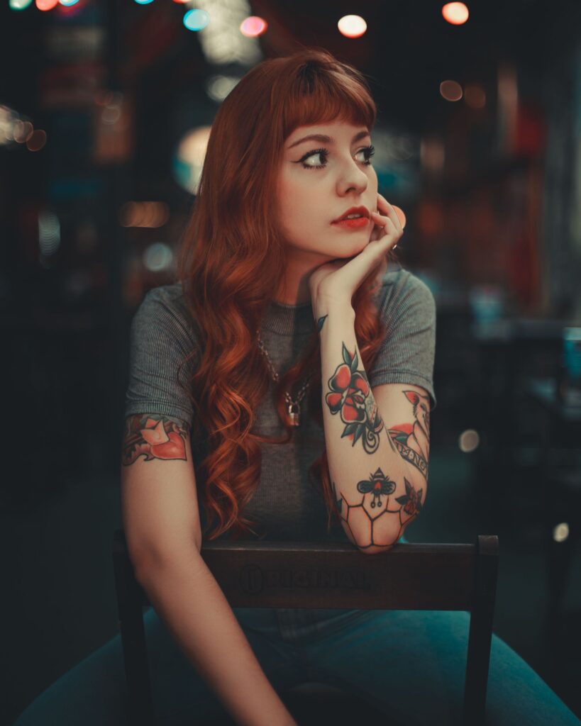 Young woman with tattoos gazes thoughtfully in dimly lit urban café.